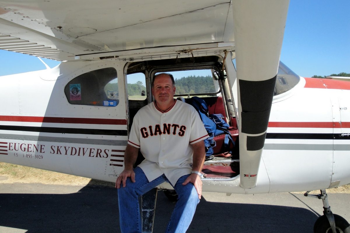 man with Giants jersey sits in the door of Eugene Skydiver's Cessna plane