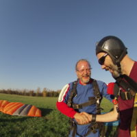 instructor shakes the hand of his skydiving student in landing area after skydive