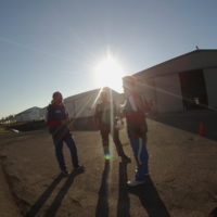 three men stand in front of the hangar while waiting to board the plane to make a tandem skydive