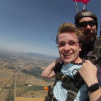 young man smiles under canopy during tandem skydive